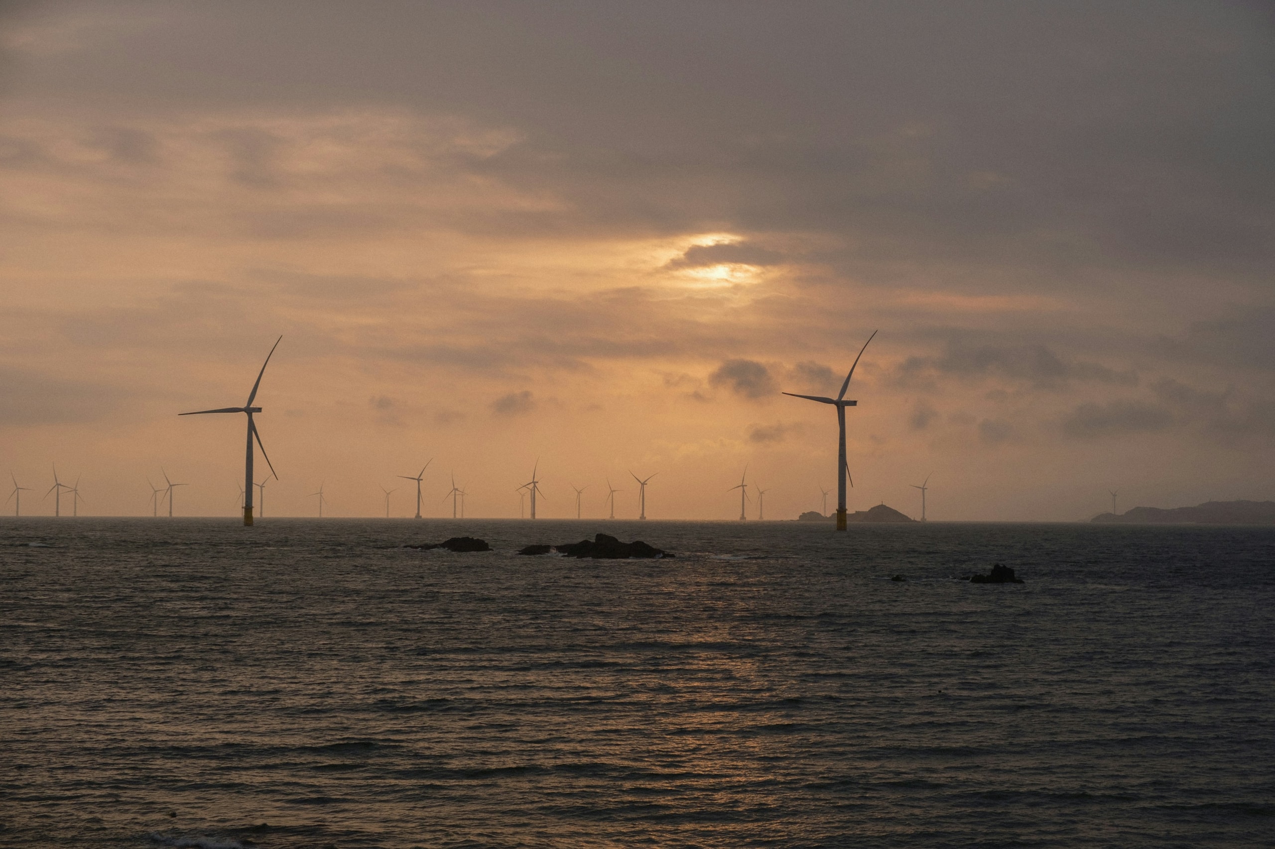 Offshore wind turbines spanning a dark sea beneath an amber sunset sky