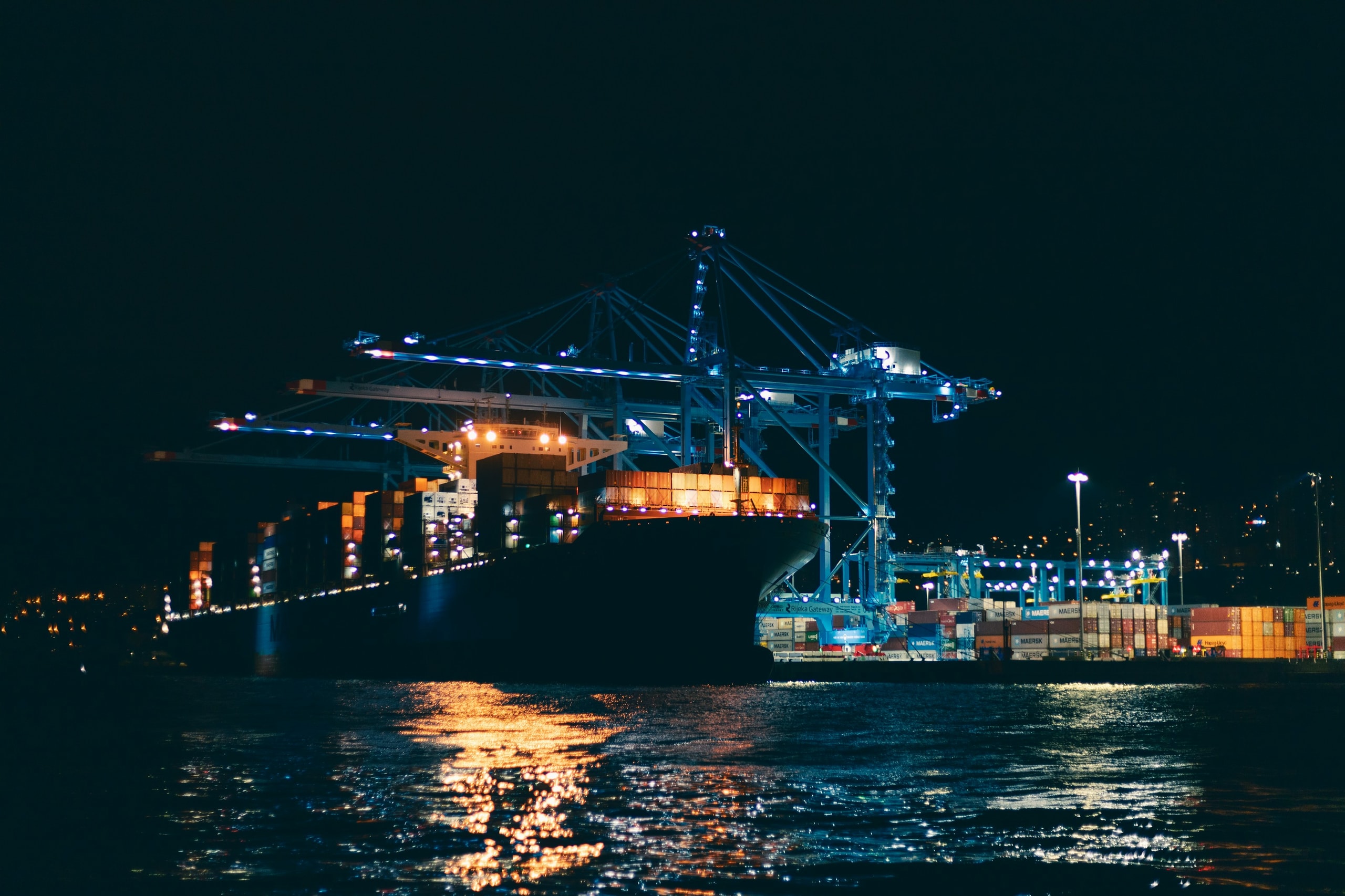A container ship being serviced by illuminated cranes at the Port of Rijeka at night