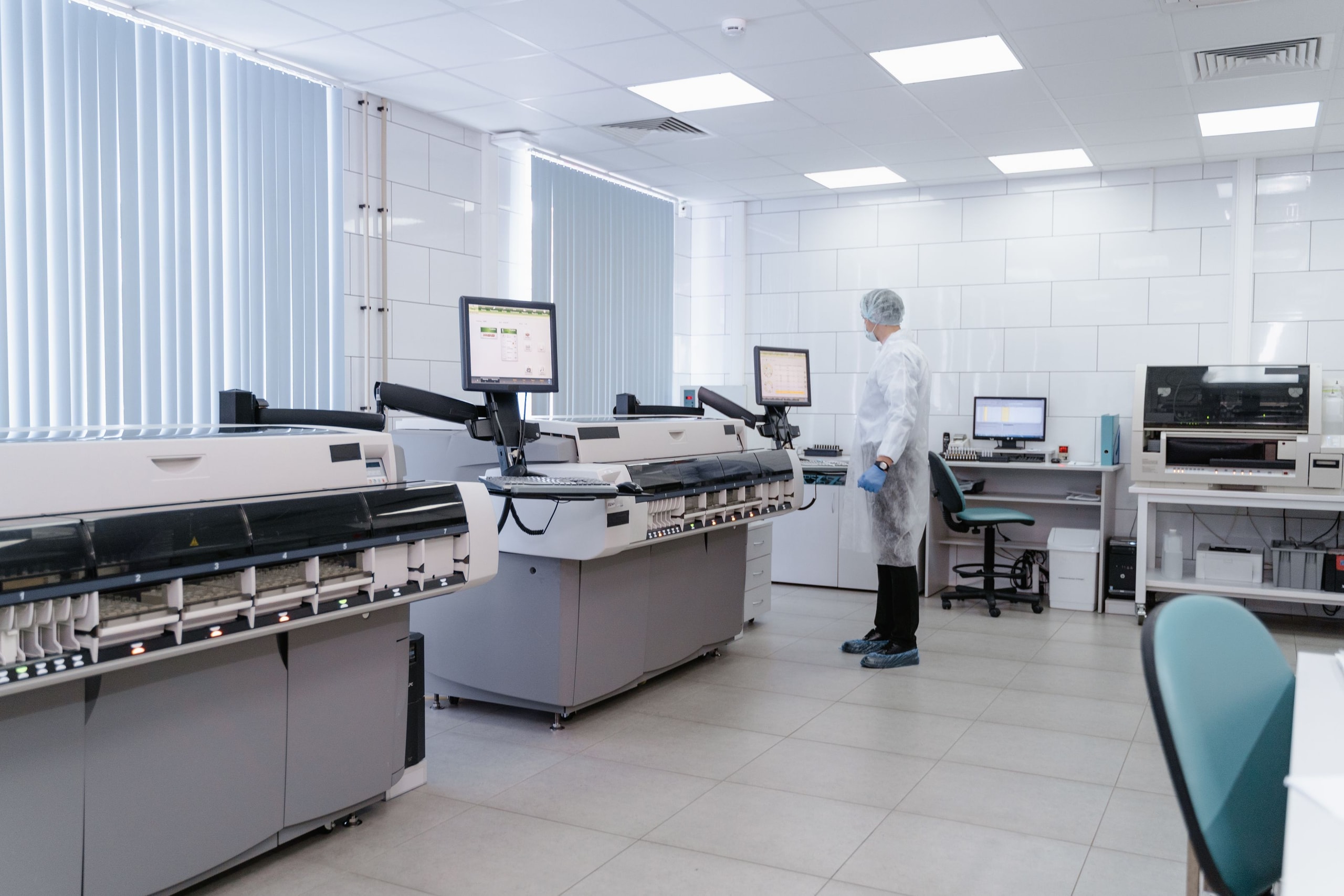 A researcher in protective clothing monitoring automated equipment in a bright clinical laboratory
