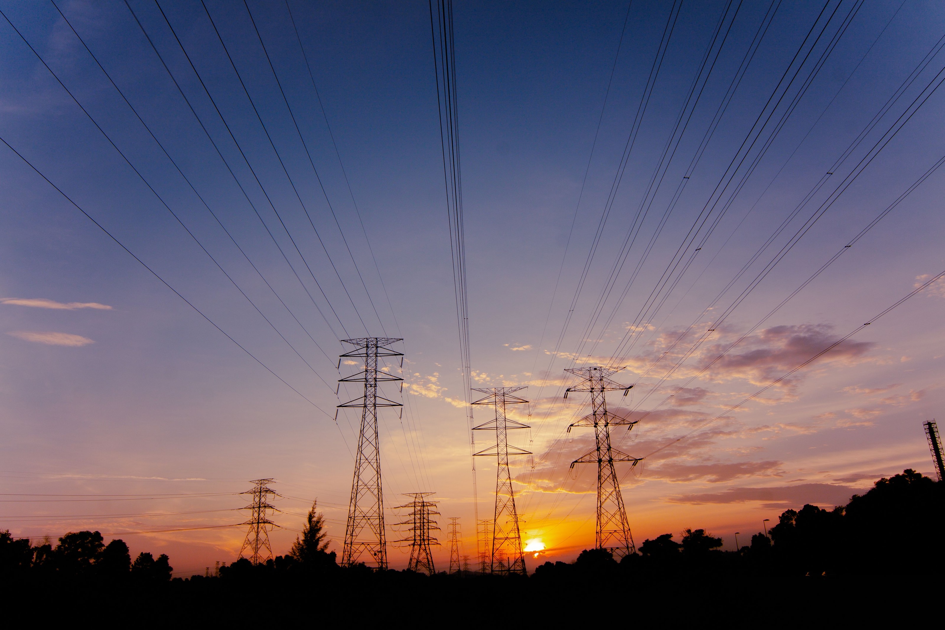 High-voltage transmission lines converging across a power grid at sunset