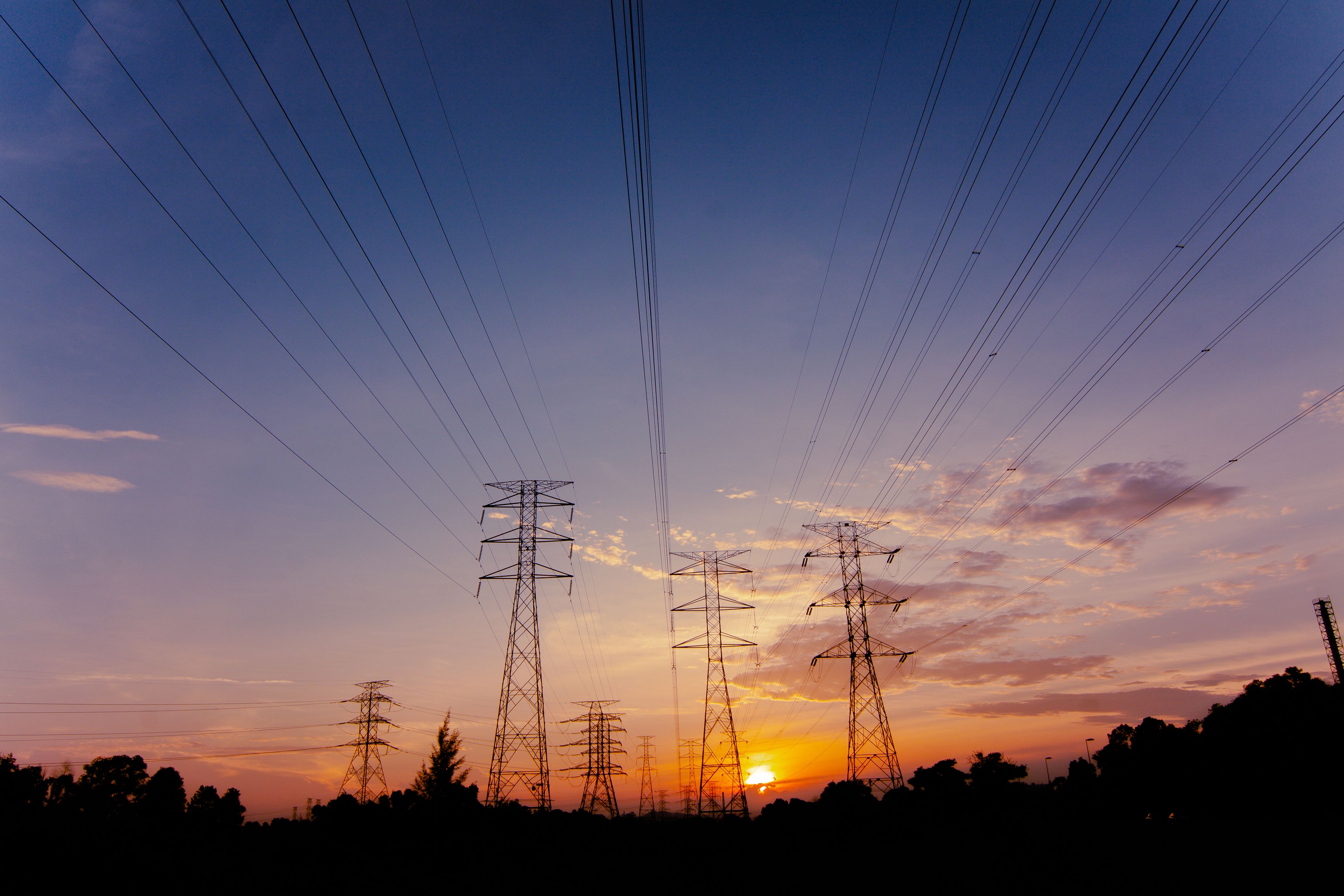 High-voltage transmission lines converging across a power grid at sunset