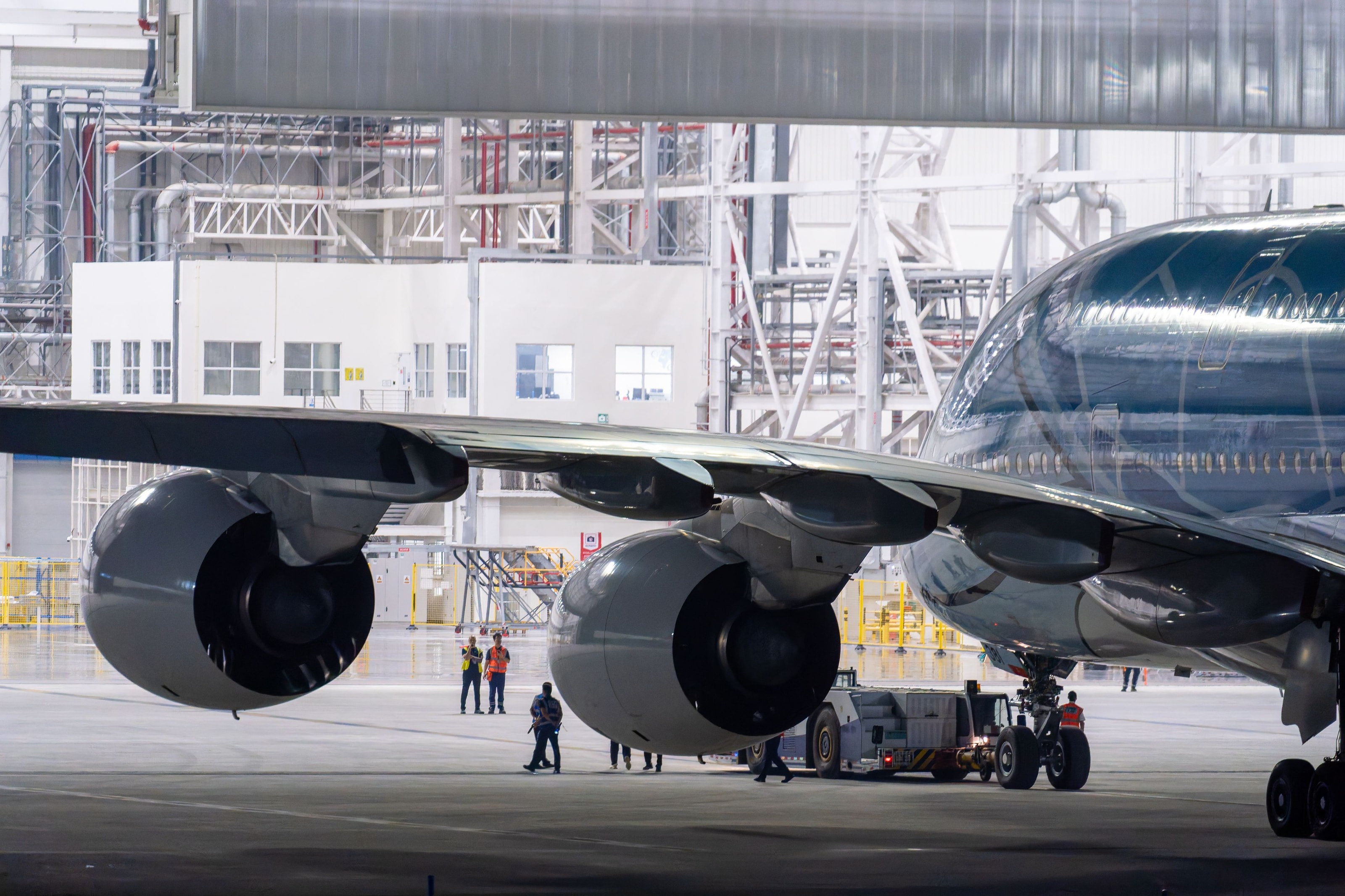 A wide-body aircraft and maintenance crew inside a bright aviation hangar