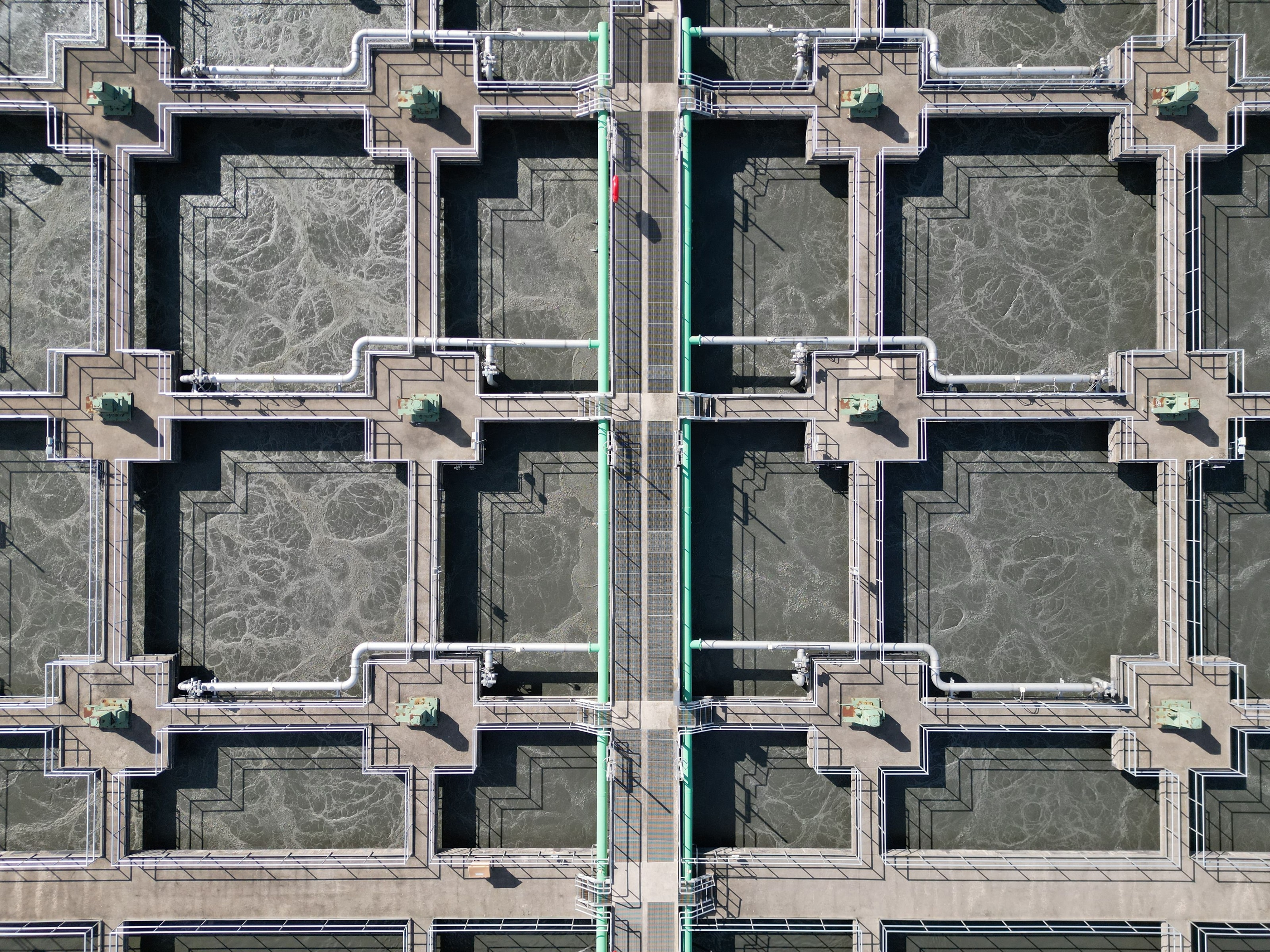 Aerial view of a municipal water treatment facility with aeration tanks, pipes, and a central service spine