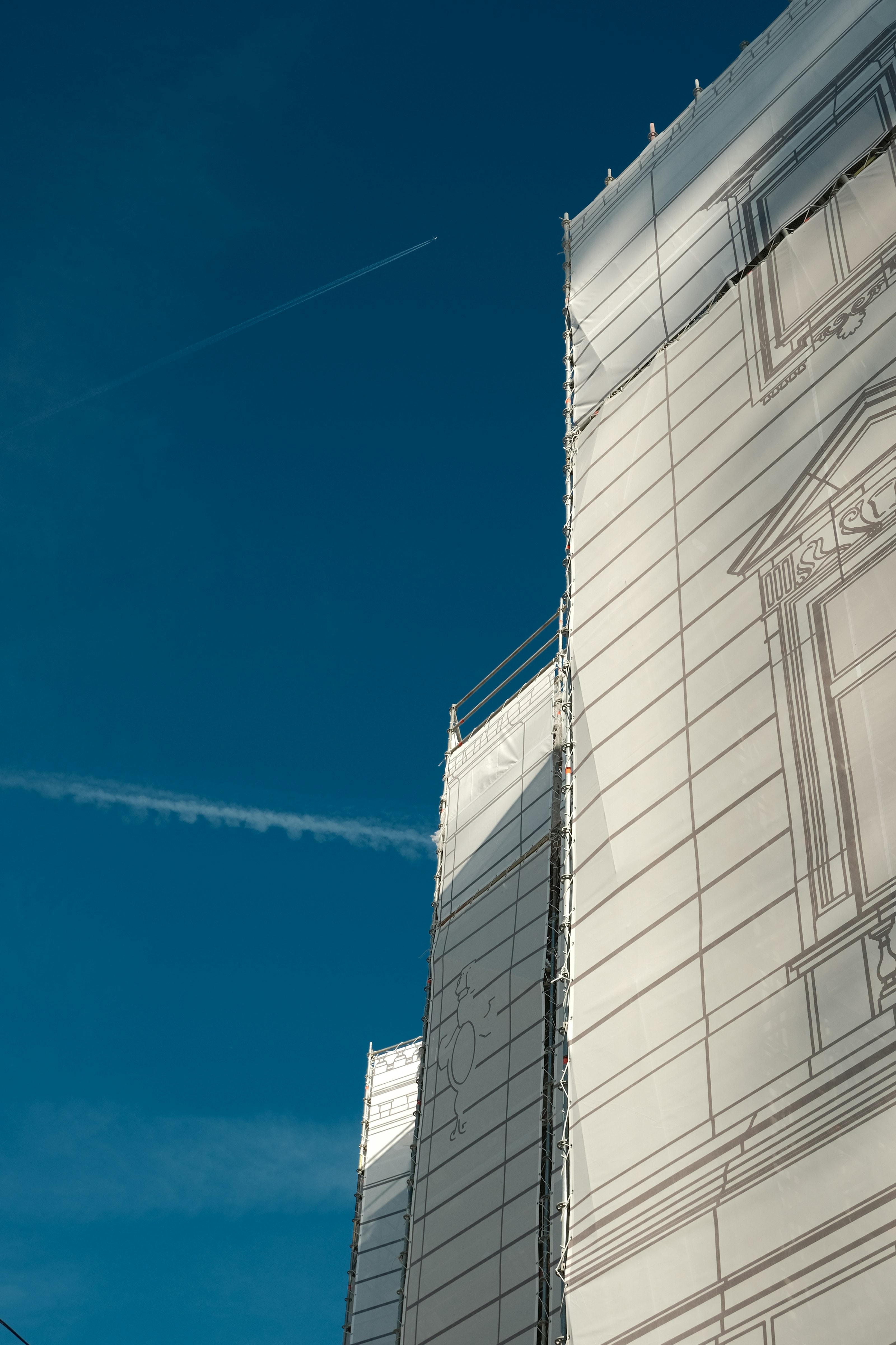 A building wrapped in printed renovation scaffolding against a deep blue sky
